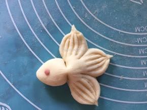 将红曲粉加入一小块面团中揉匀，再揉出一个个极小的圆形小红球，放至金鱼头部前端，当金鱼的眼睛