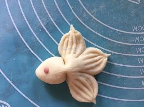 将红曲粉加入一小块面团中揉匀，再揉出一个个极小的圆形小红球，放至金鱼头部前端，当金鱼的眼睛