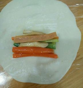 取一张饺子皮，用擀面杖擀大擀薄。放皮的三分之一处放上适量食材。
