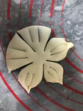 把小圆面团按扁，用切面刀均匀分成五份，但不要切断（如图），每个花瓣上浅浅划两刀，把两个角向中间捏起来，形成花瓣状