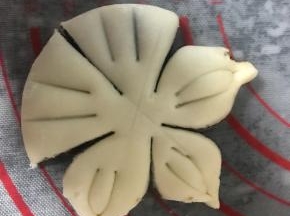 把小圆面团按扁，用切面刀均匀分成五份，但不要切断（如图），每个花瓣上浅浅划两刀，把两个角向中间捏起来，形成花瓣状