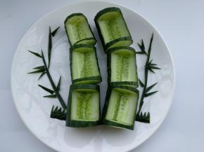 黄瓜切成差不多小段，为了摆放平稳底部削去一层皮。用小刀将黄瓜中间切空。黄瓜皮切成竹竿和竹叶，摆入餐盘。
