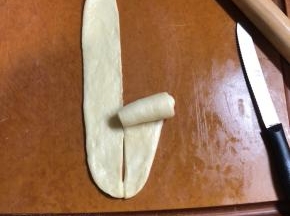 面团松弛好擀开，擀成椭圆形。翻面，用刮板把面团切开，然后把底边压薄。卷成玫瑰花形。