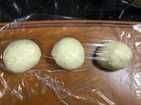 发酵完成将面团取出，排气，分割成9等份。滚圆，盖保鲜膜松弛20分钟。我这次用了两个模具。同时准备以下两项工作（忘记拍照了），模具薄薄抹上一层油，白芝麻和低分混合备用。