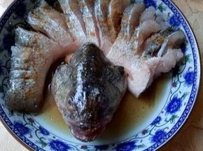 再将鲈鱼的背部切开，但不要切段，摆放再盘子里，将鱼头放在鱼的背部上面。放入料酒，盐，生抽。十三香，腌制10分钟。