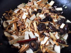 随后先放入香干片煸炒，把香干的豆腥味煸炒出去，然后放入香菇、干花菜、笋干，煸炒片刻。