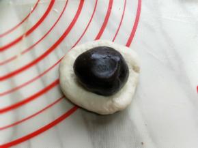 取一块面团，用手心压扁，放入豆沙馅。包起来，捏紧。