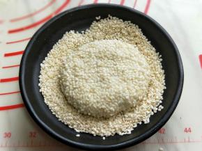 再将包好的豆沙馅饼用掌心压扁，放入白芝麻器具中，裹满白芝麻依次做完。