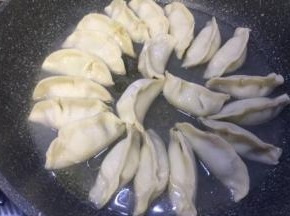 包好后全部搬放在平底锅里面，开火倒入食用油，再倒入能淹没饺子三分之一处的清水，可加盖焖
