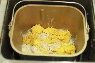 先将主面团材料（除黄油外）放入面包机桶内，将中种面团撕成小块一起放入面包机桶