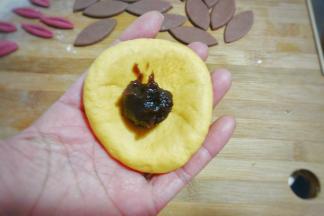 取一个黄面团用擀面杖稍微擀开，再用手凹成窝形放入适量豆沙馅