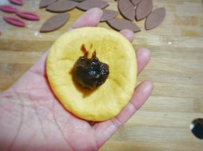 取一个黄面团用擀面杖稍微擀开，再用手凹成窝形放入适量豆沙馅