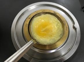 倒入一勺蛋液，轻轻地旋转，使蛋液均匀地铺满勺子。