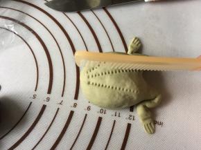 将面条如图折成青蛙腿，用锋利的刻出青蛙爪子，再用干净梳子在青蛙背上轻按压出3条细纹