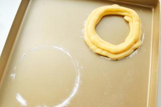 烤盘里先用一个圆形的小碗倒扣，稍微用面粉撒出一个圆环。然后沿着圆环挤出里外两条面糊，上面再挤上一条。共做了两条圆形的泡芙。剩余的泡芙面糊也别浪费了，挤在空余的地方，又烤了几个球型泡芙。