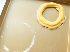 烤盘里先用一个圆形的小碗倒扣，稍微用面粉撒出一个圆环。然后沿着圆环挤出里外两条面糊，上面再挤上一条。共做了两条圆形的泡芙。剩余的泡芙面糊也别浪费了，挤在空余的地方，又烤了几个球型泡芙。