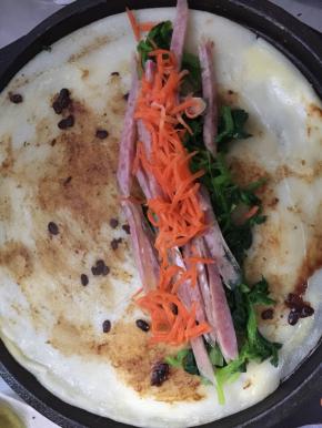 蛋液不流动时翻面，刷适量的豆瓣酱，将菠菜、肠、胡萝卜一次摆成长条状，卷起