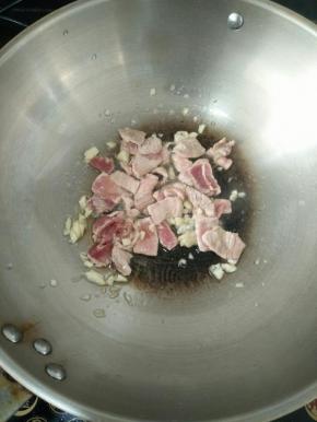 热锅凉油下蒜蓉爆香后加入猪肉和料酒，煸炒至变色。