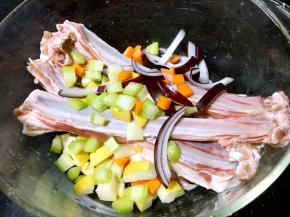 将水果和蔬菜放到盛有羊排的容器里。