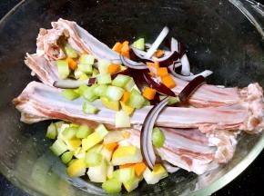 将水果和蔬菜放到盛有羊排的容器里。