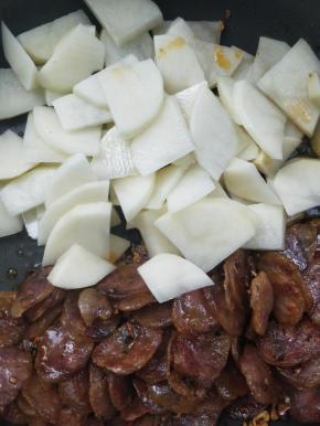 把腊肠拨到锅一边，倒入沥干水的土豆片。