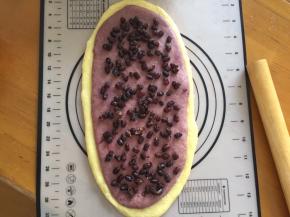 将面团擀长，紫薯面团放在原味面团上面，再铺上蜜豆，从下往上卷起