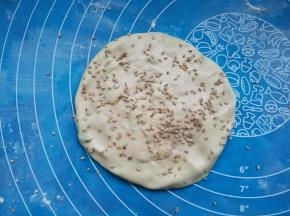 手上沾糖水，将面团推扁推圆。撒上白芝麻。