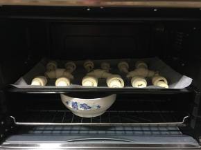 把牛角生坯放在垫有油纸的烤盘中，间隔一定的距离，放进烤箱中进行二次发酵。（烤箱中放一碗热水，保持湿润的环境，烤出来的牛角包很松软，不会很结实，发硬。）
