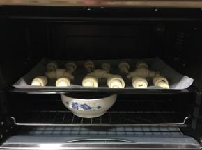 把牛角生坯放在垫有油纸的烤盘中，间隔一定的距离，放进烤箱中进行二次发酵。（烤箱中放一碗热水，保持湿润的环境，烤出来的牛角包很松软，不会很结实，发硬。）
