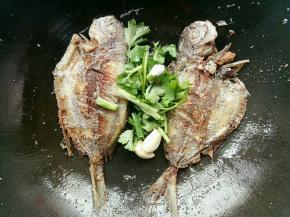 鱼煎到两面金黄的时候倒掉多的油，然后放入蒜头香菜煎一下再加入水煮，水煮开后加入一勺盐和一勺酱油煮一下