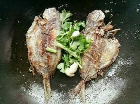 鱼煎到两面金黄的时候倒掉多的油，然后放入蒜头香菜煎一下再加入水煮，水煮开后加入一勺盐和一勺酱油煮一下