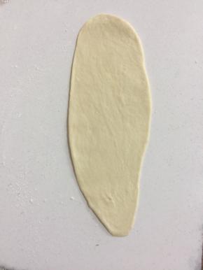 取一个面团，用手稍微按扁后翻面，用擀面杖擀成长舌状，底部压薄。