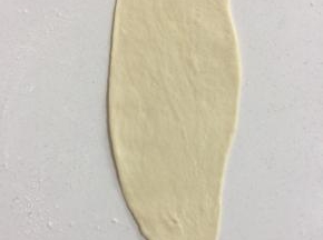 取一个面团，用手稍微按扁后翻面，用擀面杖擀成长舌状，底部压薄。
