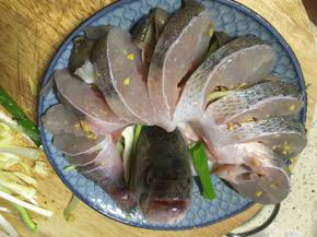 先把鱼身围成圆弧再放鱼头，放上老姜和大葱，大蒜