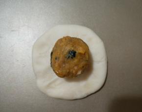 取一面团按扁，包入一个咸蛋黄肉松馅，包好，滚圆。