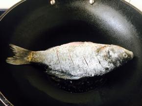 大火起锅，锅热放入少许的油，当油六成热时放入鱼，此时改中火。 煎鱼时随时微微调整火的大小，千万不要让油起烟。往油锅里放鱼时，用双手分别拎住鱼头和鱼尾，贴着油面轻轻地放入。 我使用的是不粘锅。 如果小伙伴们使用的是铁锅就要把锅烧的热热的，然后用姜在锅里涂抹一层，再继续操作。