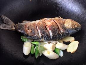 将煎好的鱼扒在锅的一边，放入葱段和姜片，煸出香味。