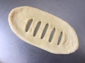 取一个面团擀成椭圆形，翻面，用刀在中间割开几条口子，割透