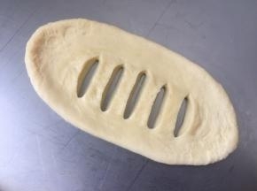 取一个面团擀成椭圆形，翻面，用刀在中间割开几条口子，割透
