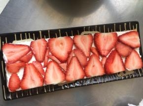 在一片蛋糕片上均匀地涂抹一层淡奶油，再摆上草莓片