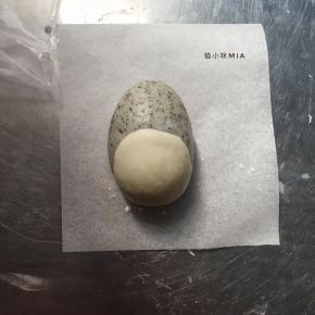 将8克的白色面团擀成圆形的状态，黑面团表面沾点牛奶，包裹在黑芝麻面团的中下部分，粘合起来