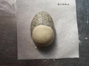 将8克的白色面团擀成圆形的状态，黑面团表面沾点牛奶，包裹在黑芝麻面团的中下部分，粘合起来