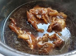 完成后从压力锅中倒入一个深盆中，这时候可以看到肉表层和牛筋都上色了。把肉继续浸泡在汤汁中放凉。