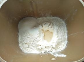 倒入面粉，尽量全部盖住牛奶液，把白糖放在面包机的一角，面粉中间挖个眼，倒入酵母，让酵母不会直接与糖和盐接触