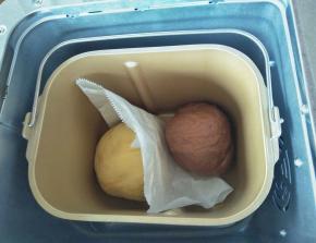 把两种颜色的面团放入面包桶，中间用一张油纸隔开，以防粘连，再按启动键，进行基础发酵