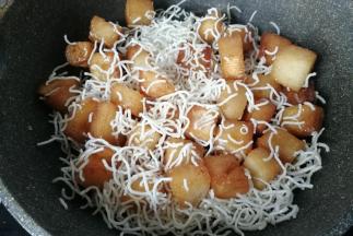 再把炸好的粉丝用手稍微捏碎后倒入锅中，让馒头丁裹上粉丝