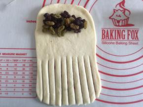 翻面然后在2/3出用刮板切出一条条口子，上面放上蜜豆和葡萄干自上而下的卷起来就可以了