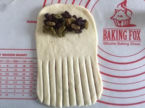 翻面然后在2/3出用刮板切出一条条口子，上面放上蜜豆和葡萄干自上而下的卷起来就可以了