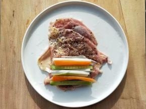 平摊开鸡腿排，依次放胡萝卜条，黄瓜条，葱段。