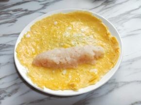 煎好的蛋饼铲出，放上麟虾肉，整理一下形状，之后从一面卷起。